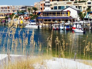 The Joint Adventure tied to the boardwalk, as seen through the dune grass on the beach across the harbor